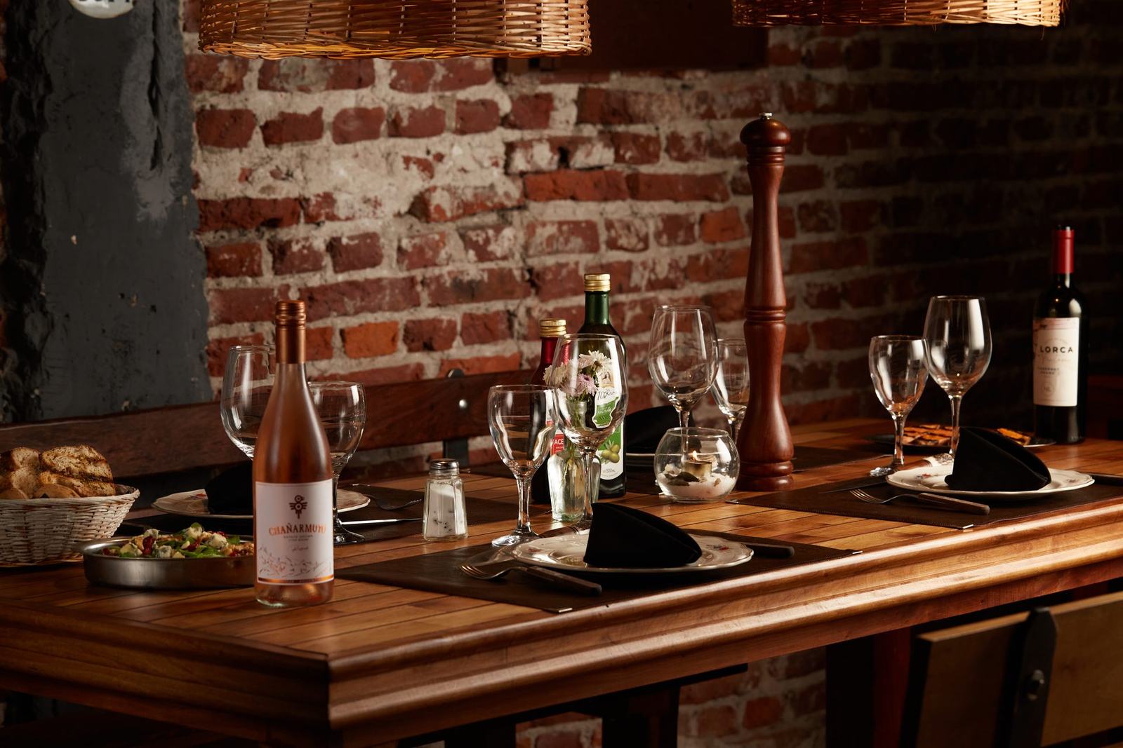 Mesa servida en Almacén de Carnes: vinos, copas y pan sobre mesa de madera con pared de ladrillo